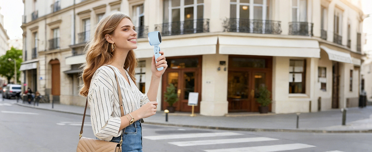 Woman walking in city holding blue handheld fan stylish mini fan for holiday travel cooling