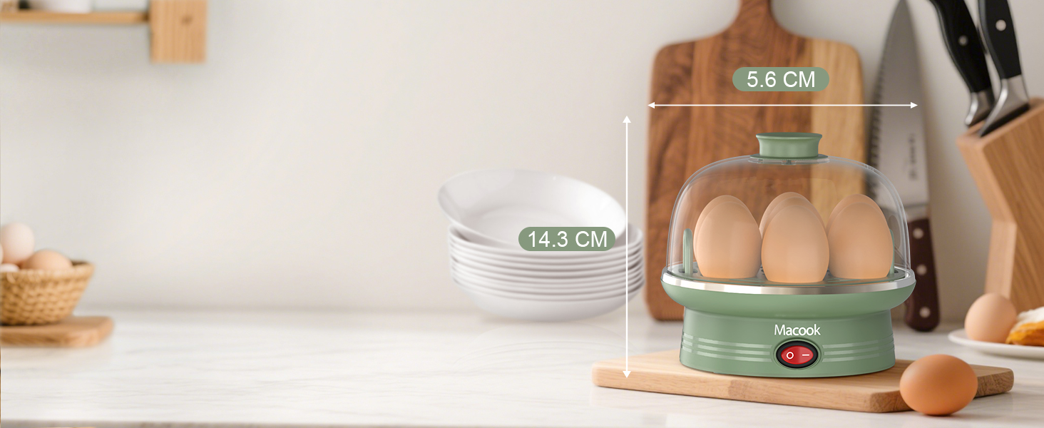 Green electric egg cooker with two tiers, holding multiple eggs. Measurements show 14.3 cm and 5.6 cm dimensions. White plates and wooden cutting board visible nearby.