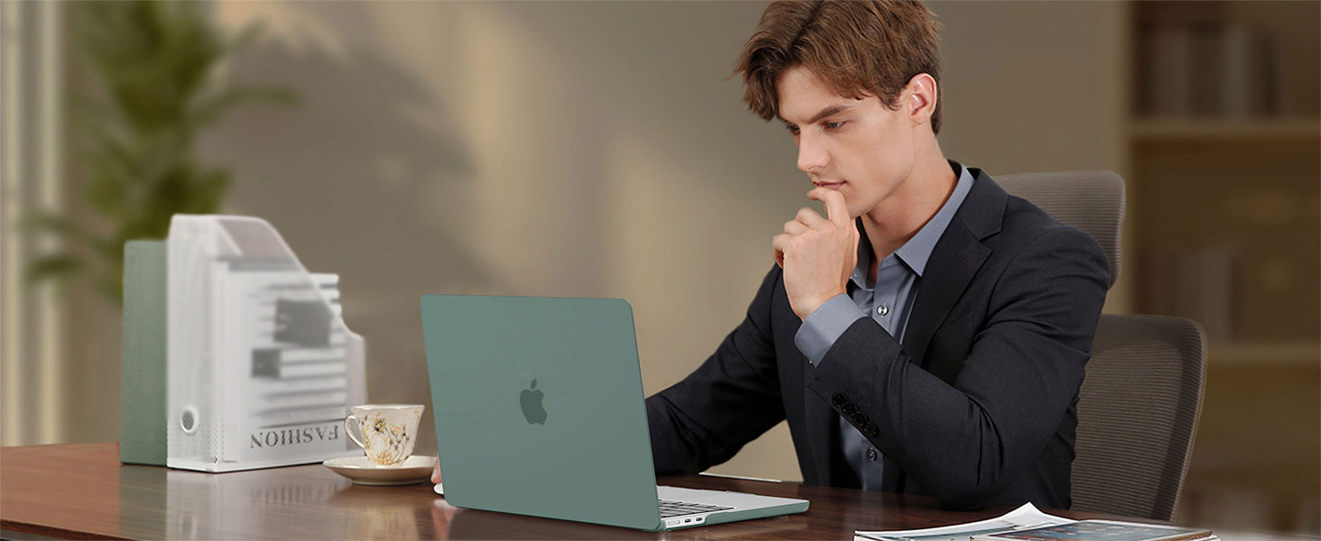 Man in suit working at desk with green laptop, white desk organizer, and coffee cup. Office setting with plant in background.