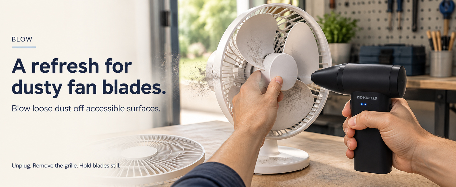 Electric air duster blowing dust off a desk fan with grille removed and blades held still