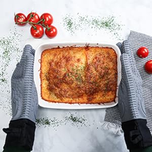 Gray silicone gloves holding a freshly baked meal with tomatoes in the background.