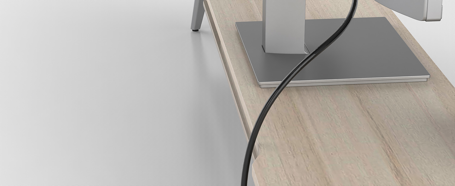 Close-up view of a black power cable against light wooden surface, partially visible electronic devices in background.