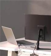 Desktop workspace with a laptop and large monitor on a white surface. A sleek black monitor arm supports the display, providing an ergonomic setup.