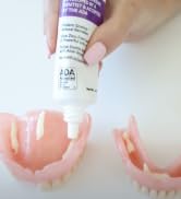hand holding tube of denture adhesive and applying to dentures