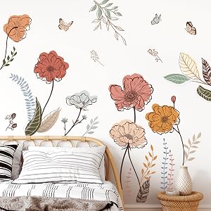 Floral wall decal featuring pastel-colored flowers, leaves, and butterflies. Shown above a white bed with woven headboard and textured pillows.