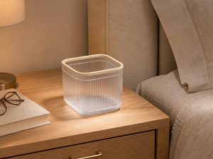 Clear mini trash can on a wooden nightstand beside a bed