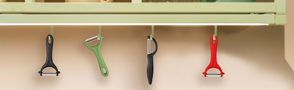 Kitchen utensil organizer with hanging peelers and tools. Four items visible: black, green, silver, and red handles against a light background.