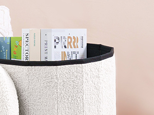 Partial view of a curved white textured surface, possibly a storage container or decorative object, with books visible in the background.