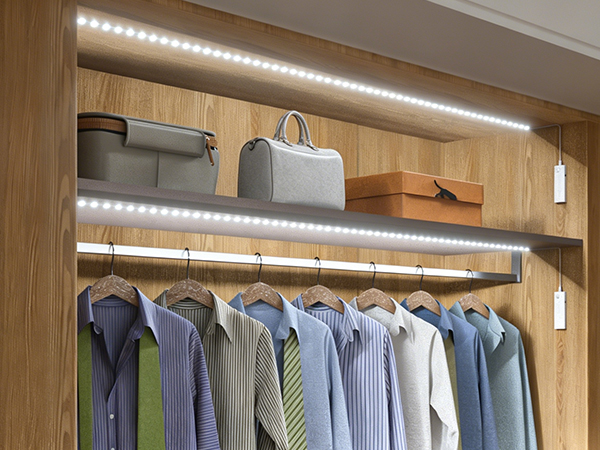 Wooden closet organization system with LED strip lighting. Multiple hanging rods display blue and neutral-toned clothing. Shelves above hold folded items and storage boxes.