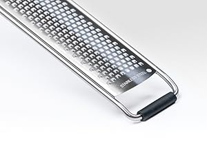 Close-up of a stainless steel grater with fine perforations. Features an ergonomic black handle and curved sides for stability.