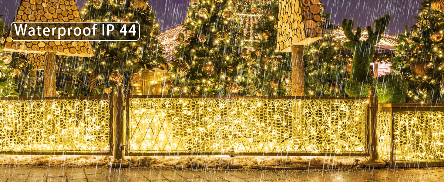 Waterproof outdoor string lights illuminating a garden fence. Warm white LEDs create a magical atmosphere in rainy conditions. IP44 rating visible.