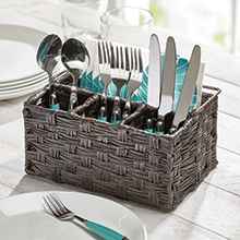 brown woven utensil caddy holding spoons, forks, knives on a white wood table, window in background