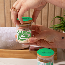 Hands holding a glass jar with a colorful printed label on the side and a round label on the lid