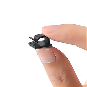 Close-up of a small, black, square-shaped object held between a thumb and index finger, possibly a camera or privacy cover.