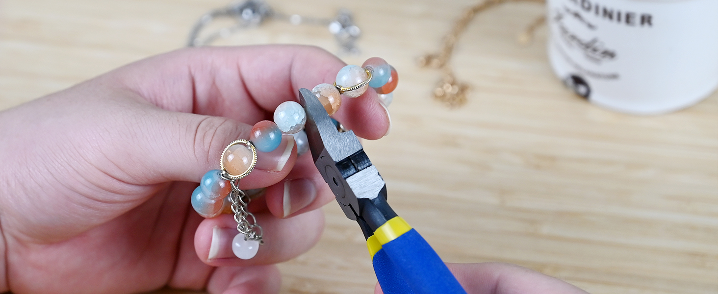 Hand holding a bracelet with colorful beads, while a yellow and black tool is used to adjust or repair it.
