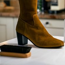 Brown suede ankle boot with block heel shown next to shoe brush on light colored surface.