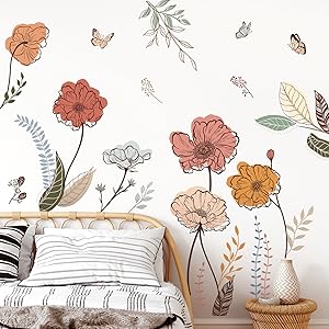 Floral wall decal featuring pastel-colored flowers, leaves, and butterflies. Shown above a white bed with woven headboard and textured pillows.