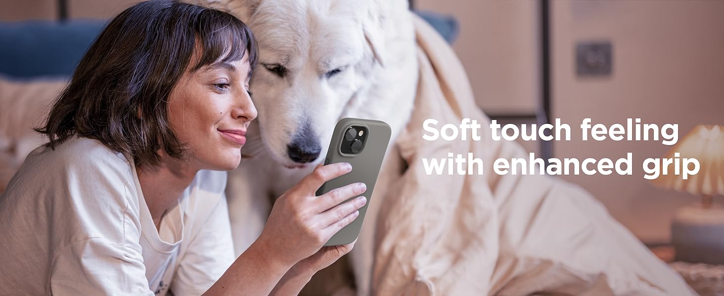Woman holding gray smartphone with enhanced grip feature, emphasizing soft touch feeling. White dog visible next to her.