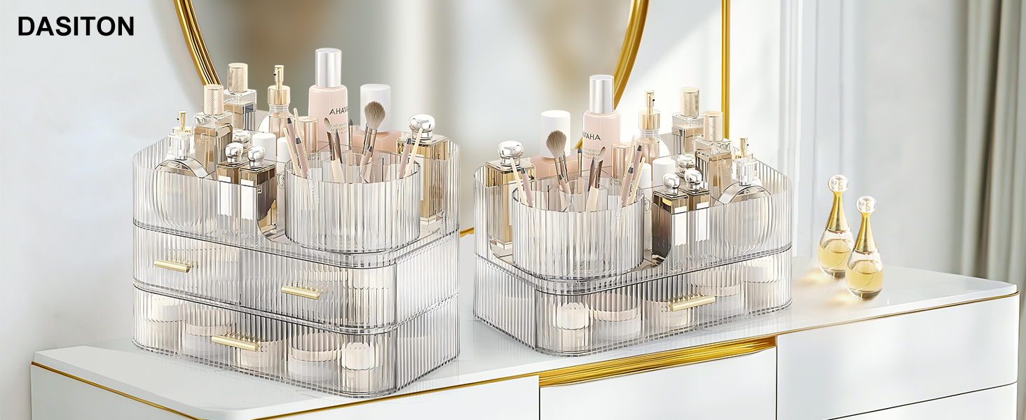 Clear acrylic makeup organizers with vertical compartments, filled with various cosmetic products including bottles, brushes, and tubes. Displayed on a white surface with gold trim.