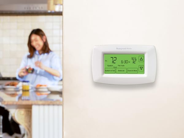 Mother and daughter in kitchen in background, thermostat on wall in foreground