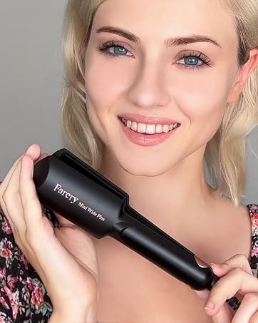 Woman with blonde hair wearing floral patterned top, holding black over-ear headphones around her neck, smiling at camera indoors.