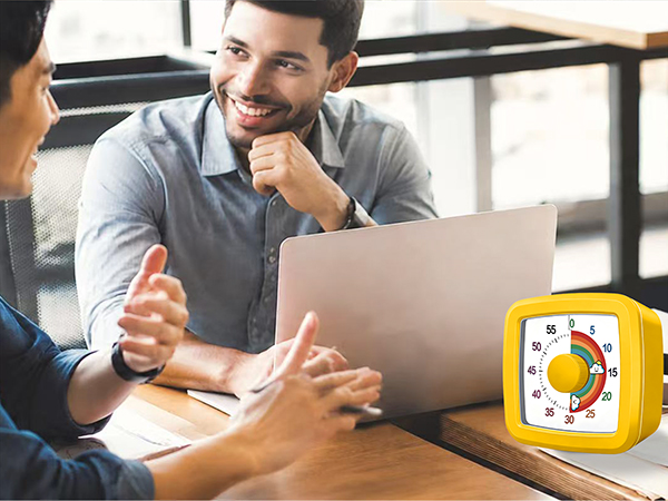 Man at laptop giving thumbs-up gesture in office setting. Yellow circular icon with chart/graph symbol in bottom right corner indicates productivity or approval.