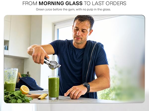 A man squeezes fresh citrus into a green smoothie in a home kitchen with an lemon press.