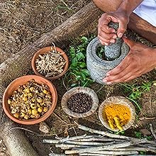 Man in nature grinding herbs with mortar and pestle with bowls of various herbs nearby