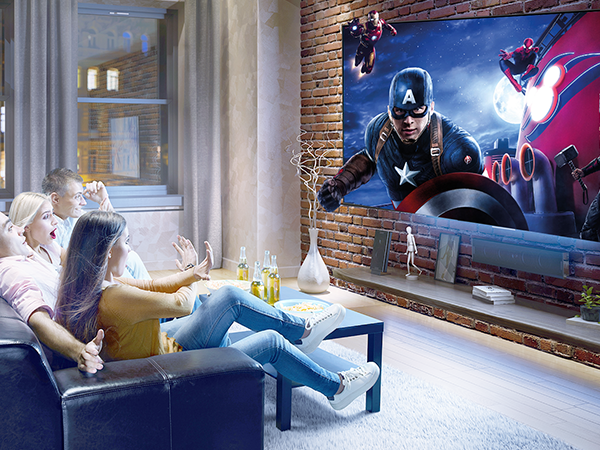 Home theater setup showing large projected movie screen on brick wall, with viewers relaxing on comfortable seating in foreground.