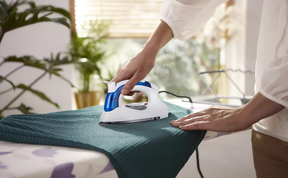 A person is ironing a coat with DenniesCare travel iron on the ironing board.