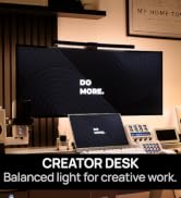 Text reads "DO MORE" and "CREATOR DESK - Balanced light for creative work." Desktop setup featuring monitor displaying text, keyboard, audio speakers, and desk lamp in modern workspace.