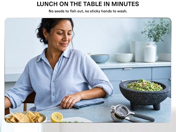 A woman sits down to lunch, with a stainless steel citrus squeezer and guacamole on the table.