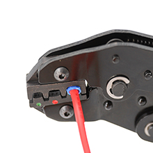 Close-up of a black metal tool or device with red wire, featuring a circular dial and several buttons or connectors.