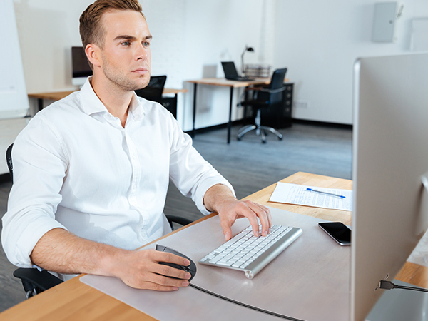 Modern office setting with a computer workstation featuring a wireless keyboard and mouse on a wooden desk.