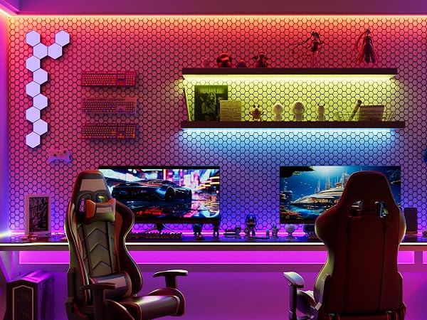 Gaming setup with two racing-style chairs, large monitor, hexagonal wall lights, and shelves with decorative items. Room illuminated by vibrant purple and blue LED lighting.