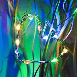 Heart-shaped string lights glowing against a blurred, colorful background. Thin wire with small LED bulbs forms the heart outline.