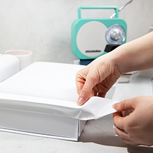 A pair of hands using white colored duct tape to seal a white box on a light marble countertop
