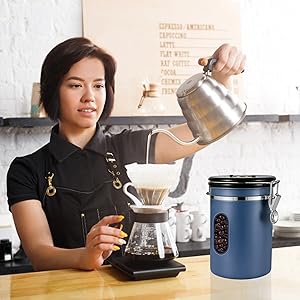 Coffee brewing setup with a gooseneck kettle, pour-over dripper, and glass carafe. A blue canister with a window showing coffee beans is visible.