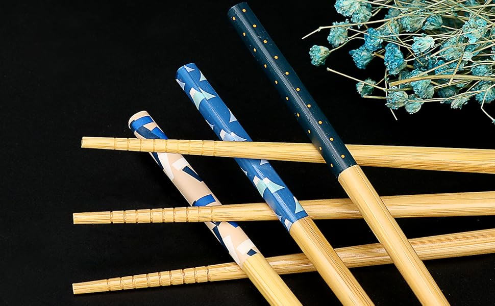Set of wooden chopsticks with blue and white patterns. Dried blue flowers in background on black surface.