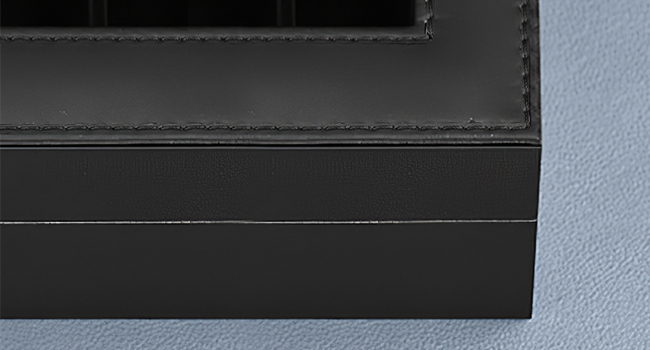 Close-up detail of black textured surface with linear edge detail, appears to be part of electronic device or furniture piece.