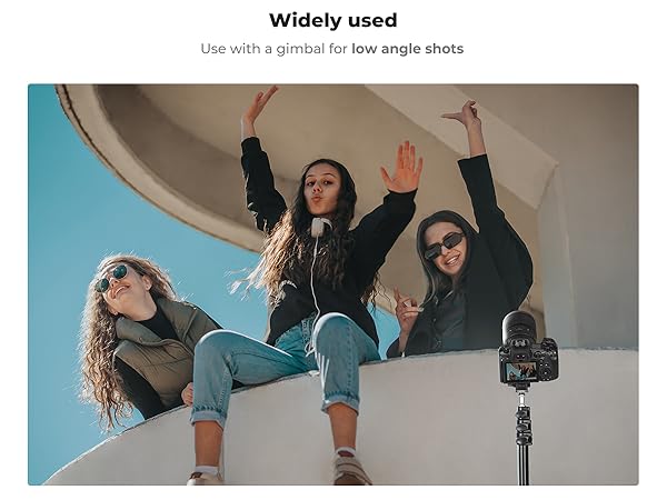 Camera on tripod positioned for low-angle shot of three people on elevated surface. Demonstrates use of gimbal for capturing dynamic, wide-angle scenes from below.