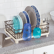 bronze dish drying rack holding dishes on marble counter, drain spout, water dripping into sink