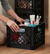 Hand placing teal organizer with toiletries inside a black milk crate
