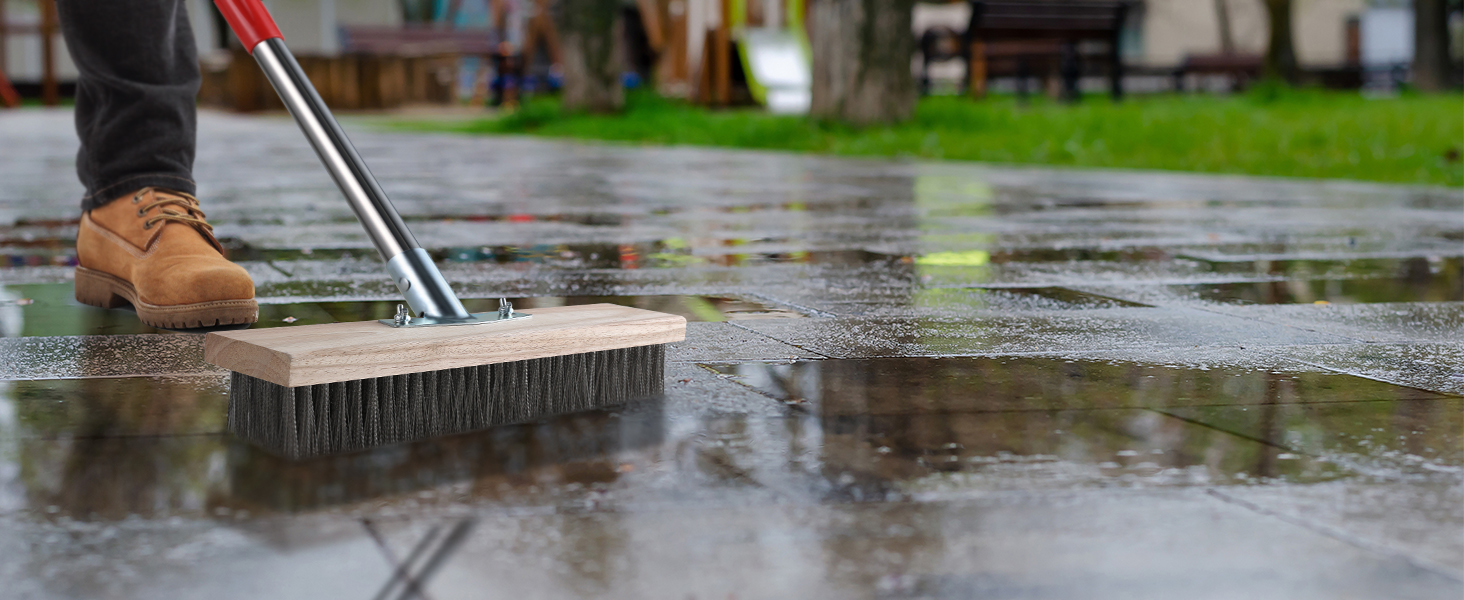 Wide push broom being used to sweep water on wet concrete surface, showing cleaning action in outdoor setting.