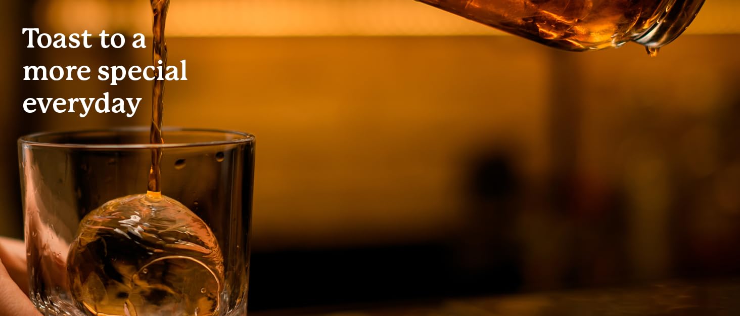 whiskey being poured down into a glass with large ice sphere