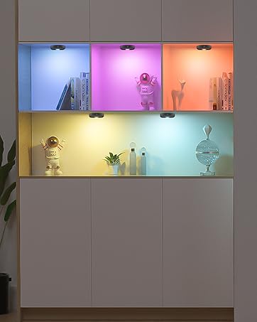Display cabinet with six backlit cubbies in different colors, showcasing various decorative items and plants. Cabinet has white doors below the display area.