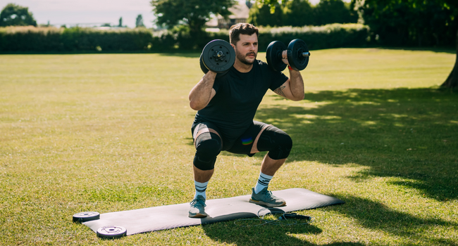 Man squatting in a park holding weights in Knee Sleeves