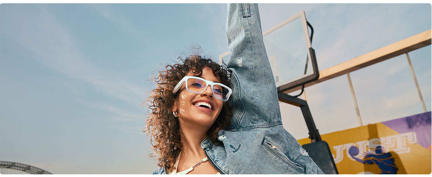 Low angle shot of a person wearing sunglasses against blue sky background, capturing joyful expression with denim visible.