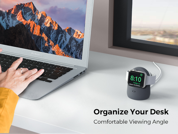 Desk setup with laptop displaying mountain scene. Small charging stand holds smartwatch showing time. Text overlay reads 'Organize Your Desk, Comfortable Viewing Angle'.