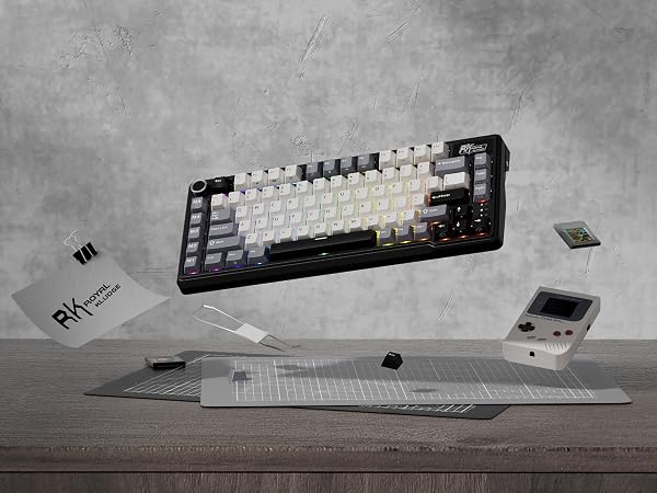 Mechanical keyboard with white and black keycaps on a desk, accompanied by small electronic devices and paper materials.